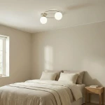 Lampa sufitowa Sopra z dwoma kulistymi kloszami w kolorze białym, mocowana na metalowej ramie w odcieniu mokka. Ujęcie z góry, umieszczona w jasnym wnętrzu sypialnym nad łóżkiem z pościelą w neutralnych kolorach.