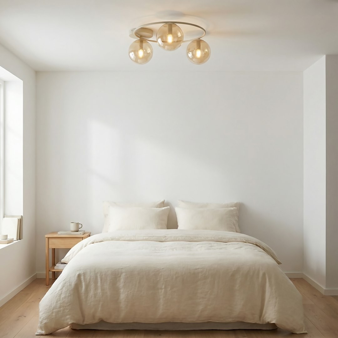 Lampa sufitowa Sopra 3xE14 w kolorze mokka i bursztynowym, z okrągłą metalową podstawą i trzema szklanymi kloszami. Zawieszona w jasnym wnętrzu nad łóżkiem, na tle białych ścian i drewnianej podłogi.