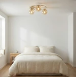 Lampa sufitowa Sopra 3xE14 w kolorze mokka i bursztynowym, z okrągłą metalową podstawą i trzema szklanymi kloszami. Zawieszona w jasnym wnętrzu nad łóżkiem, na tle białych ścian i drewnianej podłogi.