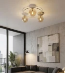 Lampa sufitowa Sopra 3xE14 w kolorze mokka z bursztynowymi kloszami, zamontowana na okrągłej podstawie. Widoczna w nowoczesnym wnętrzu z szaro-betonową ścianą, z kanapą i dekoracyjnym obrazem w tle.