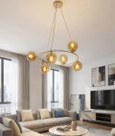 Lampa wisząca Azura w kolorze mokka i bursztynu, z sześcioma szklanymi kulami na złotym stelażu. Wisi w nowoczesnym wnętrzu, oświetlając przestrzeń. Kule mają przezroczyste wykończenie, a całość zawieszona jest na długich linkach.