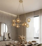 Lampa wisząca Azura w kolorze mokka z bursztynowymi kloszami, zawieszona na trzech cienkich linkach. Osiem źródeł światła E14 w okrągłych, przezroczystych kloszach tworzy nowoczesny efekt. Tło przedstawia stół z zastawą i dekoracjami w jasnych tonach.