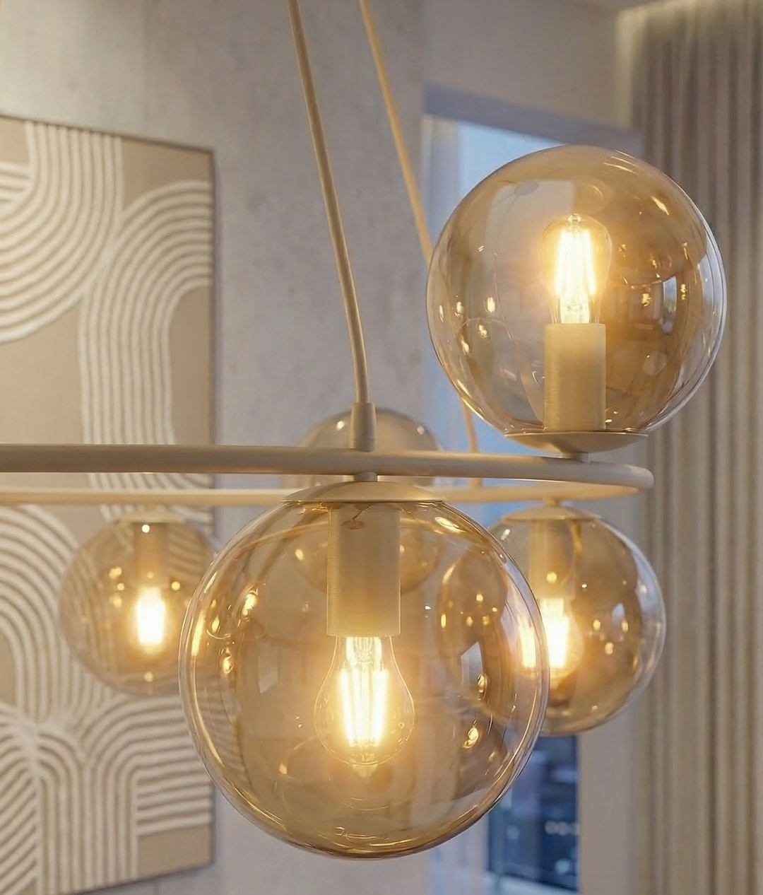 Lampa wisząca Azura z osiemnastoma żarówkami E14 w kolorze mokka i bursztynu. Posiada okrągłe, przezroczyste klosze, które emitują ciepłe światło. Zawieszona na cienkich kablach, w nowoczesnym wnętrzu, z jasnym tłem.