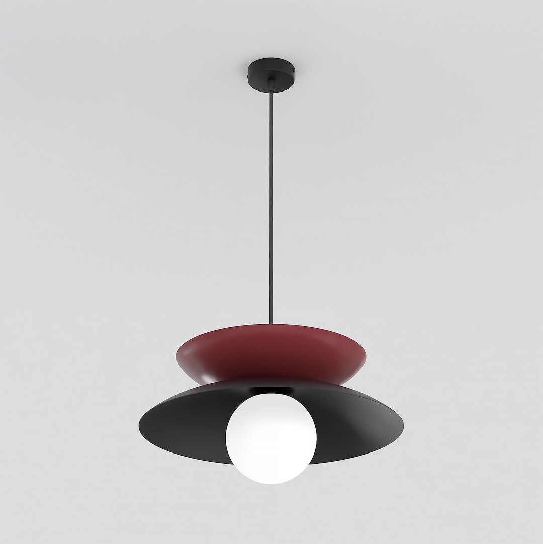Lampa wisząca Nagoya 1xG9 w kolorze czarnym i burgundowym. Posiada okrągłą, białą żarówkę, umieszczoną między dwoma płaskimi kloszami – czarnym na dole i burgundowym na górze. Zawieszona na cienkim czarnym przewodzie, wisi z sufitu.