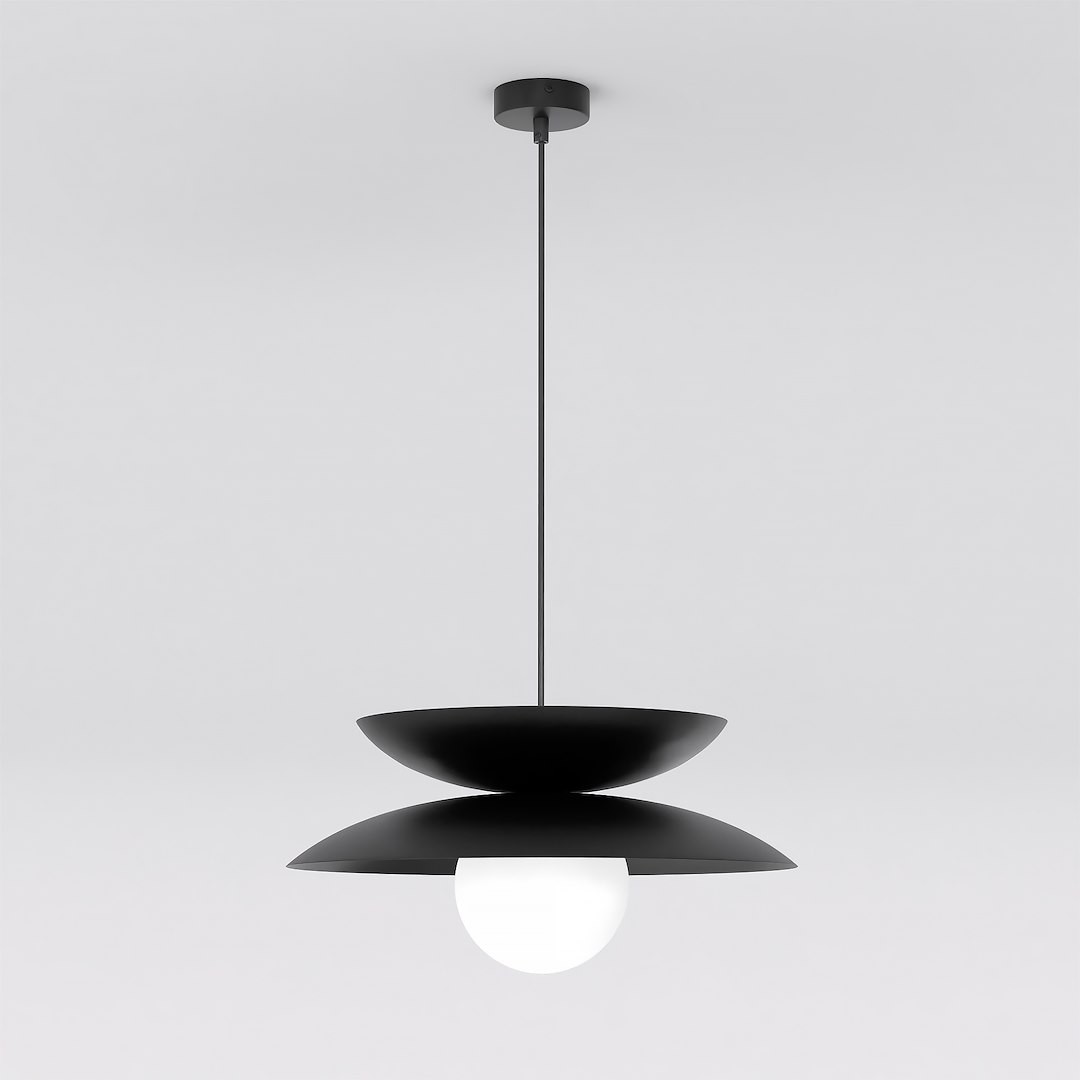Czarna lampa wisząca Nagoya z jednym źródłem światła G9, z okrągłą, białą kulą umieszczoną pomiędzy dwoma poziomymi, czarnymi talerzami. Lampa zawieszona na cienkim przewodzie, z zamocowaniem sufitowym. Proste tło.