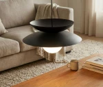 Lampa wisząca Nagoya 1xG9 w kolorze czarnym, składająca się z dwóch okrągłych, matowych osłon oraz wbudowanej żarówki w kształcie kuli. Zawieszona nad drewnianym stołem, w tle widoczna kanapa i zasłony.