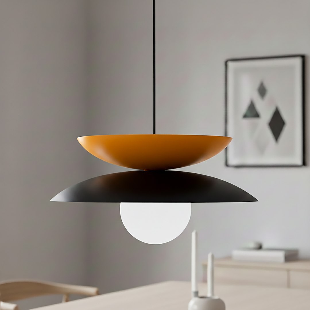 Lampa wisząca Nagoya z czarnym i pomarańczowym kloszem, z białą kulistą żarówką. Zawieszona na cienkim, czarnym przewodzie, w nowoczesnym wnętrzu. Klosze mają kształt talerza, górny pomarańczowy, dolny czarny, co tworzy efektowną kompozycję.