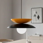 Lampa wisząca Nagoya z czarnym i pomarańczowym kloszem, z białą kulistą żarówką. Zawieszona na cienkim, czarnym przewodzie, w nowoczesnym wnętrzu. Klosze mają kształt talerza, górny pomarańczowy, dolny czarny, co tworzy efektowną kompozycję.