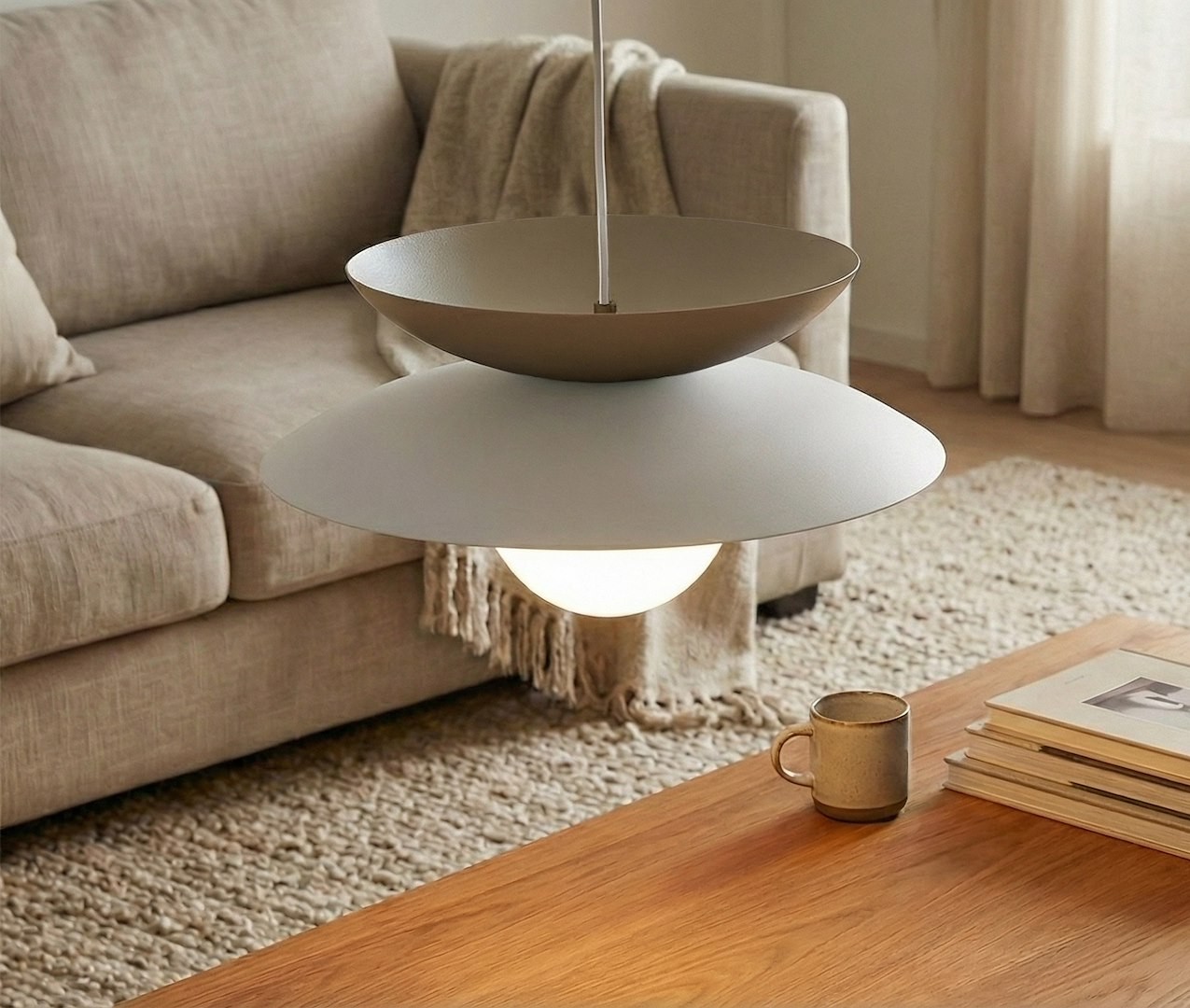 Lampa wisząca Nagoya 1xG9 w kolorze białym i mokka, zawieszona nad drewnianym stolikiem. Posiada dwa okrągłe klosze: górny w kolorze mokka i dolny biały, z widoczną żarówką. Tło to jasny salon z kanapą i dywanem.