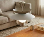 Lampa wisząca Nagoya 1xG9 w kolorze białym i mokka, zawieszona nad drewnianym stolikiem. Posiada dwa okrągłe klosze: górny w kolorze mokka i dolny biały, z widoczną żarówką. Tło to jasny salon z kanapą i dywanem.