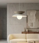 Lampa wisząca Nagoya 1xG9 w kolorze białym i mokka, z okrągłym kloszem. Ujęcie frontalne, zawieszona nad jasną sofą w nowoczesnym wnętrzu, z betonową ścianą w tle i minimalistycznymi dekoracjami.