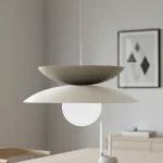 Lampa wisząca Nagoya z białym i mokka kloszem, o okrągłym, matowym kształcie, z centralną kulistą żarówką. Zawieszona na cienkim kablu w minimalistycznym wnętrzu, w tle widoczne drewniane meble i dekoracje.