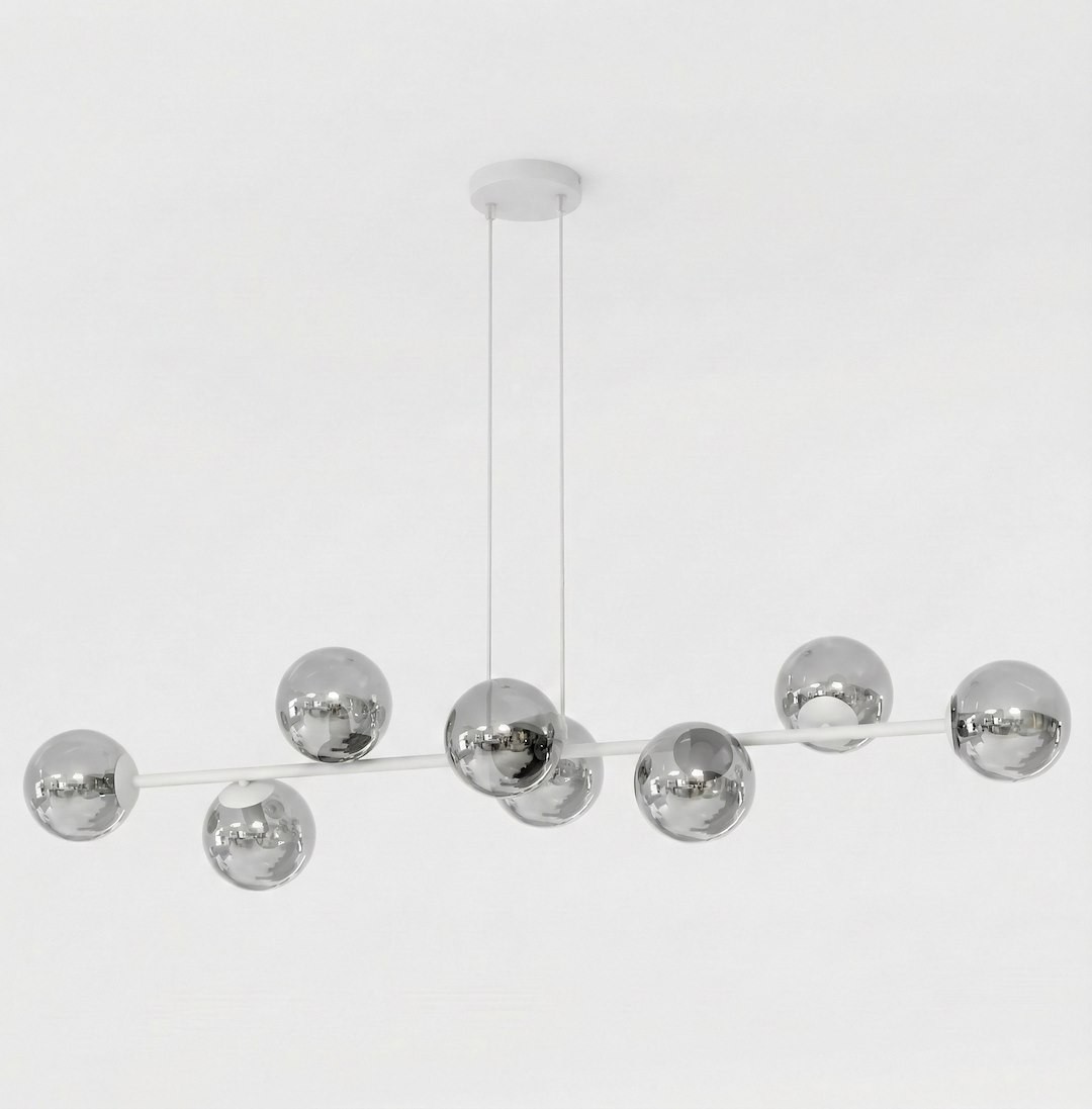 Lampa wisząca Magnus z 8 miejscami na żarówki E14 w kolorze szarym i grafitowym. Zawieszona na dwóch cienkich linkach, z ośmioma metalicznymi kulami, które odbijają światło, umieszczona na prostym stelażu. Tło białe.