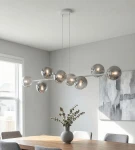 Lampa wisząca Magnus z 8 kloszami E14 w kolorze szarym i grafitowym, zawieszona na białym stelażu. Klosze w formie kul o lustrzanej powierzchni. Idealna do nowoczesnych wnętrz. Widoczna w aranżacji nad drewnianym stołem.