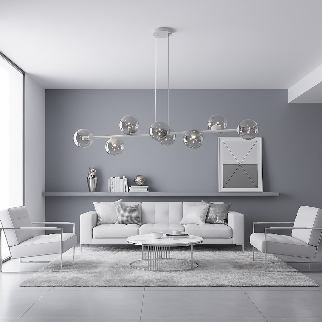 Lampa wisząca Magnus, szara/grafitowa, z ośmioma kloszami E14, zawieszona nad białą sofą w nowoczesnym wnętrzu. Klosze szklane, okrągłe, umieszczone na prostym, metalowym ramieniu. Tło szare, minimalistyczne, z dekoracjami na półce.