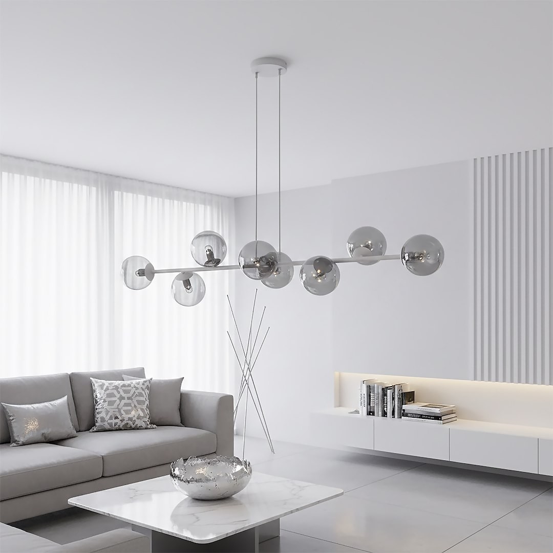 Lampa wisząca Magnus z 8 kloszami E14 w odcieniach szaro-grafitowych, zawieszona na cienkich kablach. Klosze mają okrągły kształt, wykonane z transparentnego materiału, w eleganckim, nowoczesnym wnętrzu z jasnymi zasłonami i minimalistycznym meblami.