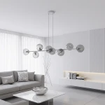 Lampa wisząca Magnus z 8 kloszami E14 w odcieniach szaro-grafitowych, zawieszona na cienkich kablach. Klosze mają okrągły kształt, wykonane z transparentnego materiału, w eleganckim, nowoczesnym wnętrzu z jasnymi zasłonami i minimalistycznym meblami.