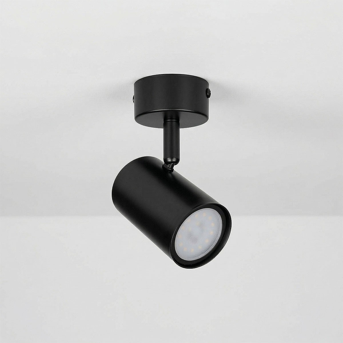 Lampa sufitowa spot GU10 w kolorze czarnym, zamontowana na okrągłej podstawie. Cylindryczny kształt oprawy skierowany lekko w dół, z widocznym źródłem światła LED. Prosty, nowoczesny design na jednolitym tle.