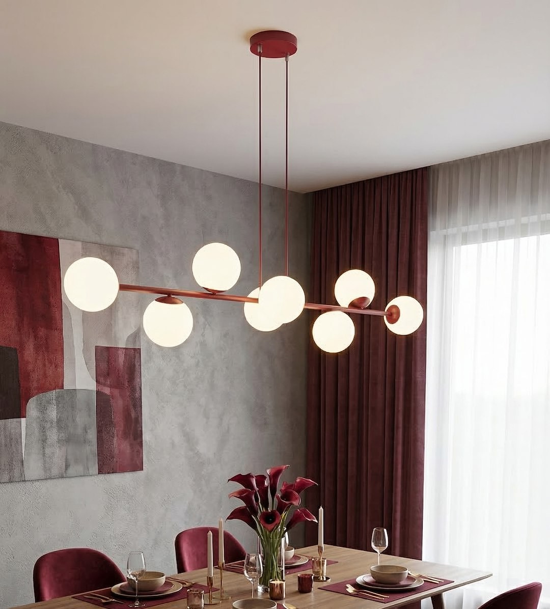 Lampa wisząca Magnus 8xE14 w kolorze burgundowym i białym, z okrągłymi kloszami, zawieszona na cienkich linkach. Widok z boku w aranżacji jadalni, z drewnianym stołem i czerwonymi akcentami, w tle zasłony i dekoracyjne obrazy.