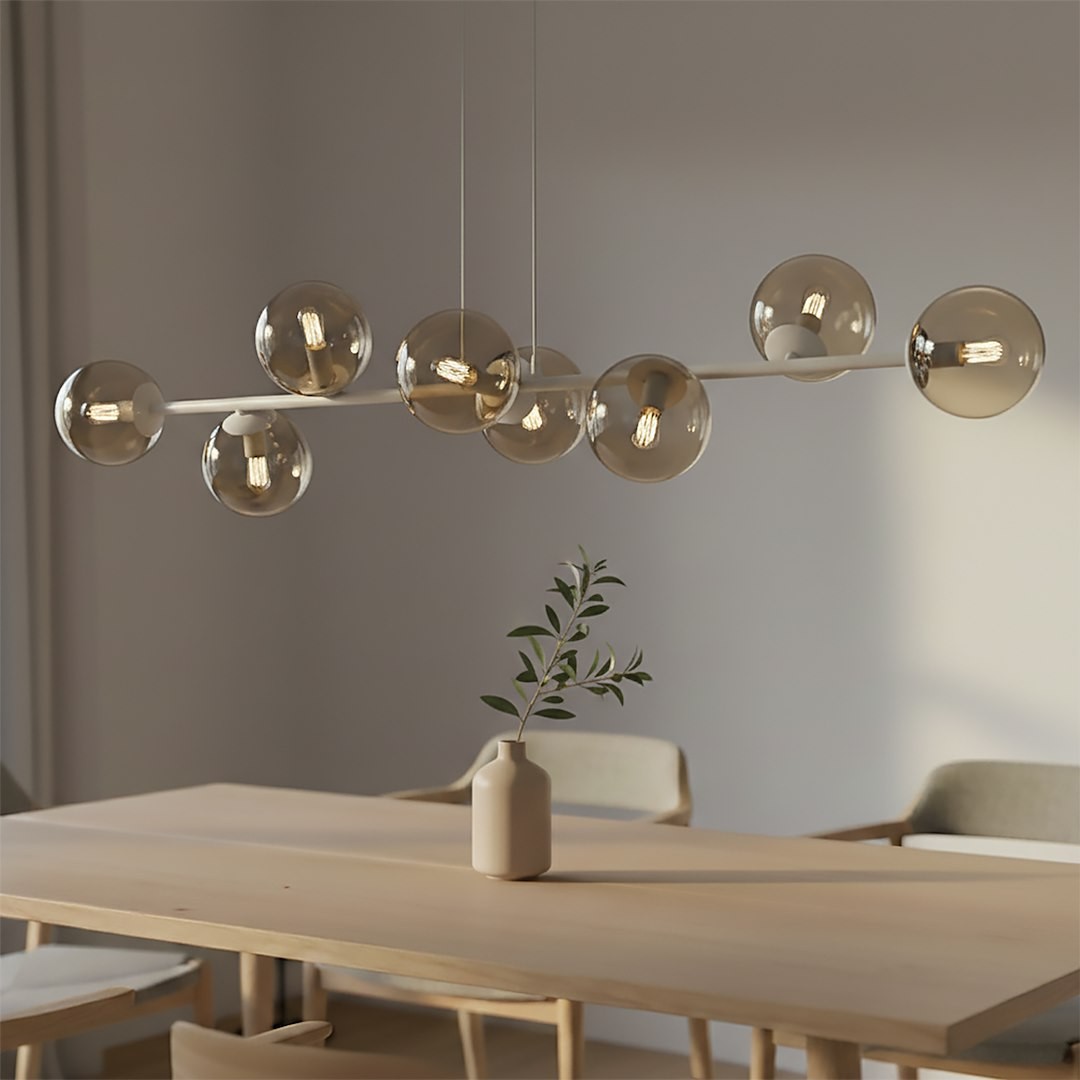 Lampa wisząca Magnus z 8 kulistymi kloszami w kolorze mokka i bursztynu, zawieszona nad drewnianym stołem. Klosze umieszczone na prostej, białej rurze, w tle widoczna wazon z gałązką. Jasne, minimalistyczne wnętrze.