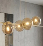 Lampa wisząca Magnus w kolorze mokka/bursztyn, z ośmioma kulistymi kloszami, zawieszona na prostym, białym stelażu. Klosze mają przezroczystą, lekko złotawą fakturę, emitując ciepłe światło. Ujęcie z bliska, skupiające się na detalach lampy.