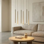 Lampa wisząca Selter 6xG9 w kolorze mokka, składająca się z sześciu długich, prostokątnych elementów emitujących ciepłe światło. Zawieszona nad okrągłym drewnianym stolikiem w nowoczesnym wnętrzu z szarym sofą i dekoracyjnym wazonem.