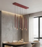 Lampa wisząca Selter 6xG9 w kolorze burgundowym, z sześcioma prostokątnymi źródłami światła zawieszonymi na cienkich linkach. Montaż sufitowy, umieszczona nad drewnianym stołem w nowoczesnym wnętrzu z szarymi ścianami i zasłonami.