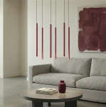 Lampa wisząca Selter 6xG9 w kolorze burgundowym, składająca się z sześciu smukłych, pionowych elementów zawieszonych na cienkich linkach. Umieszczona nad okrągłym stolikiem w nowoczesnym wnętrzu z szarym sofą i akcentami w odcieniach burgunda.