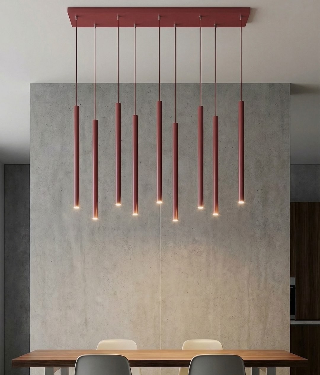 Lampa wisząca Selter 9xG9 w kolorze burgundowym, składająca się z dziewięciu smukłych, pionowych rur zawieszonych na cienkich linkach. Oświetlenie skierowane ku dołowi, montowane na prostokątnej podstawie. W tle betonowa ściana i drewniany stół.