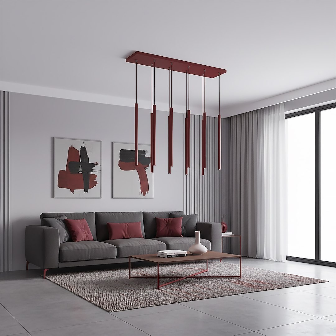 Lampa wisząca Selter 9xG9 w kolorze burgundowym, składająca się z długich, cienkich słupków zawieszonych na prostokątnej podstawie. Umieszczona w nowoczesnym wnętrzu z szarym sofą, stolikiem kawowym i dekoracjami.