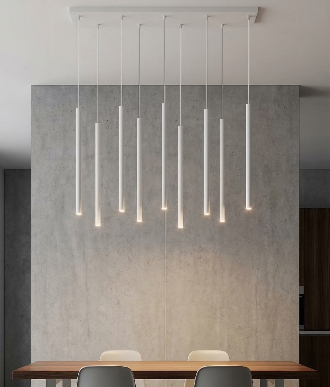 Lampa wisząca Selter 9xG9 w kolorze szarym, z dziewięcioma prostymi, cylindrycznymi kloszami, zawieszona na białym stelażu. Wisi nad drewnianym stołem w nowoczesnym wnętrzu z szarymi ścianami.