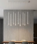 Lampa wisząca Selter 9xG9 w kolorze szarym, z dziewięcioma prostymi, cylindrycznymi kloszami, zawieszona na białym stelażu. Wisi nad drewnianym stołem w nowoczesnym wnętrzu z szarymi ścianami.