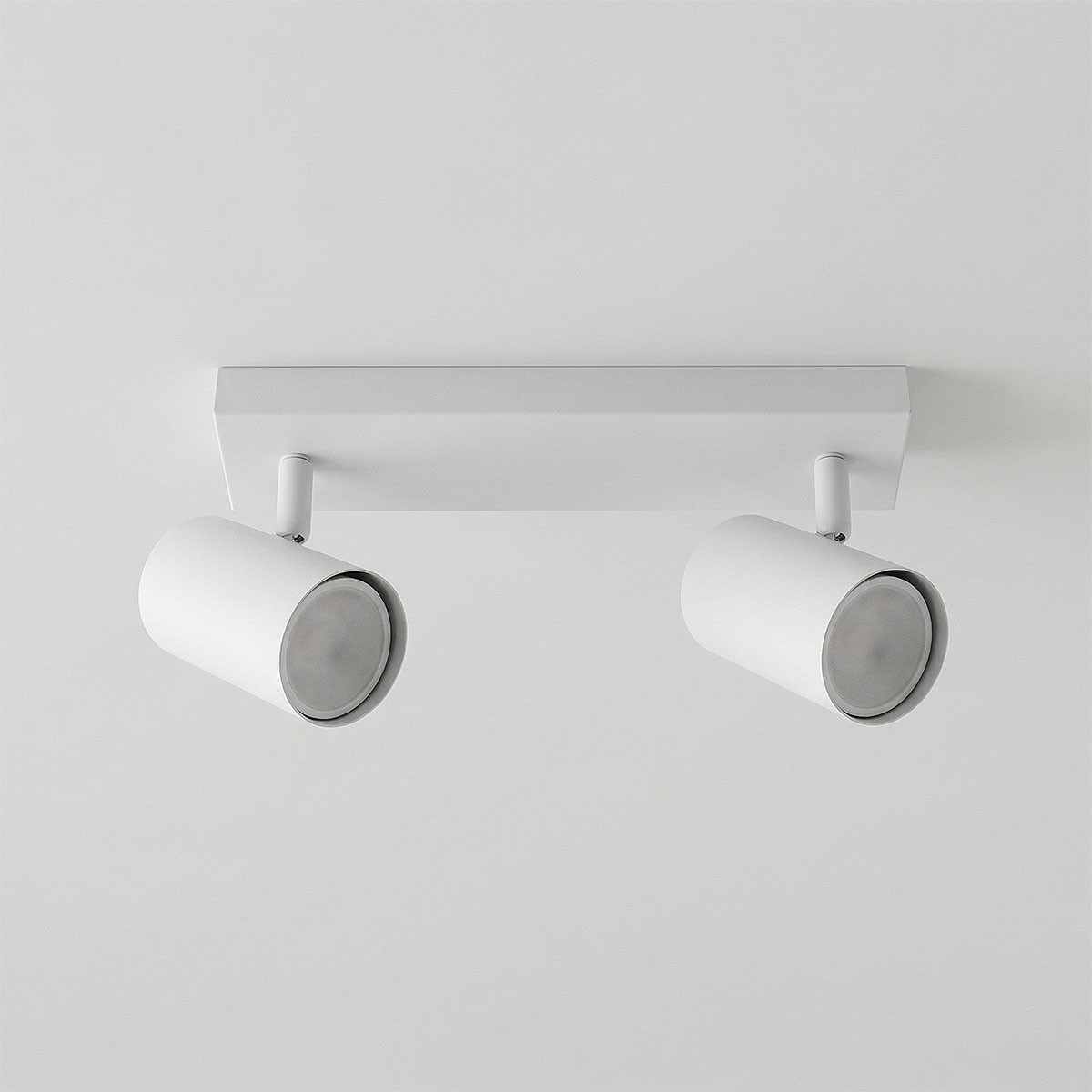 Lampa sufitowa Richi z dwoma reflektorami GU10 w kolorze białym, montowana na prostokątnej podstawie. Reflektory mają cylindryczny kształt z metaliczną obręczą, skierowane w różnych kierunkach. Tło jasne, minimalistyczne.