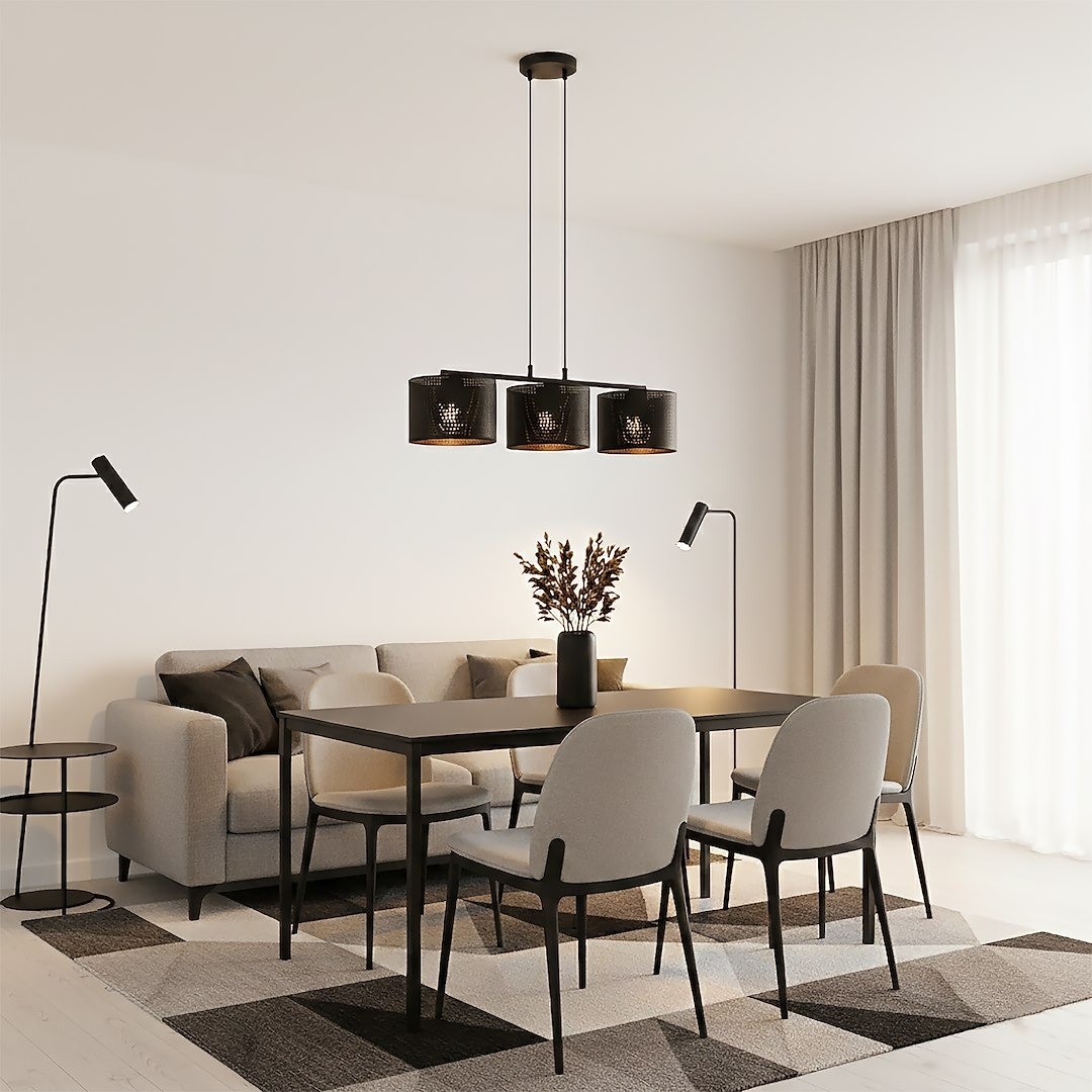 Lampa wisząca Lux 3xE27 w kolorze czarnym, z trzema cylindrycznymi kloszami. Ujęcie z dołu, zawieszona nad stołem w jadalni, otoczona jasnymi krzesłami i sofą. Tło jasne, z zasłonami, tworzy elegancki, nowoczesny klimat.