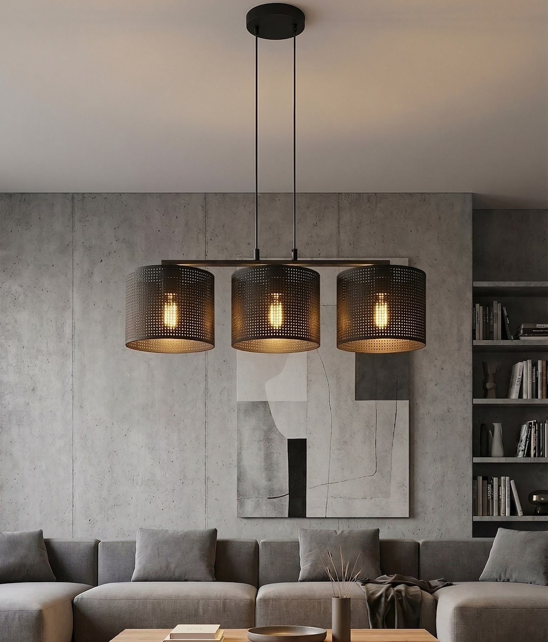 Lampa wisząca Lux z trzema kloszami E27 w kolorze czarnym, zawieszona na długich linkach. Klosze z perforowanej metalowej siatki, emitujące ciepłe światło. Lampa umieszczona nad sofą w nowoczesnym wnętrzu z szarymi ścianami i minimalistycznym wystrojem.