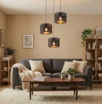 Lampa wisząca Lux 3xE27 w kolorze czarnym, z trzema cylindrycznymi kloszami. Ujęcie frontalne, zawieszona nad sofą w przytulnym salonie. W tle drewniane meble i rośliny, na stole książki i filiżanka.