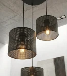 Lampa wisząca Lux 3xE27 w kolorze czarnym, z trzema cylindrycznymi kloszami z perforowanego metalu, zawieszona na długich linkach. Widoczne żarówki emitują ciepłe światło, a całość ma nowoczesny design, idealna do wnętrz.