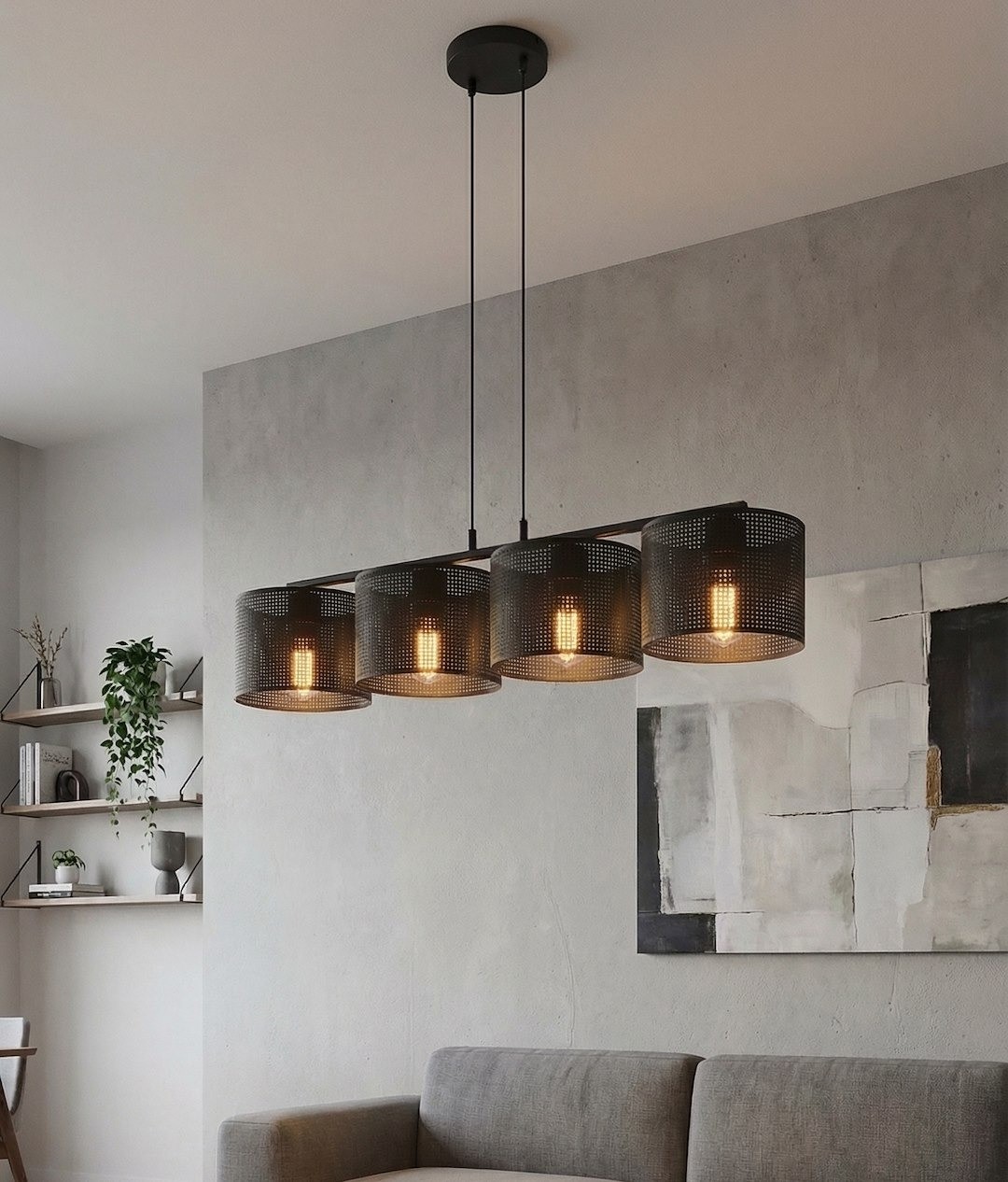 Lampa wisząca Lux w kolorze czarnym, z czterema okrągłymi kloszami z perforowanego metalu, zawieszona na cienkich linkach. Klosze odsłaniają żarówki E27, tworząc nowoczesny wygląd. Zainstalowana w aranżacji z szarymi ścianami i sofą.