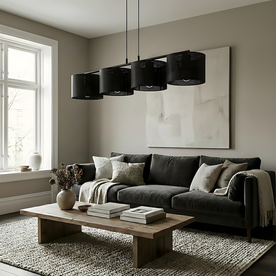 Czarna lampa wisząca Lux 4xE27 zawieszona nad stołem w nowoczesnym wnętrzu. Składa się z czterech okrągłych kloszy z perforowanego materiału, zwisających na cienkich linkach. W tle widoczna szara ściana i ciemna sofa.