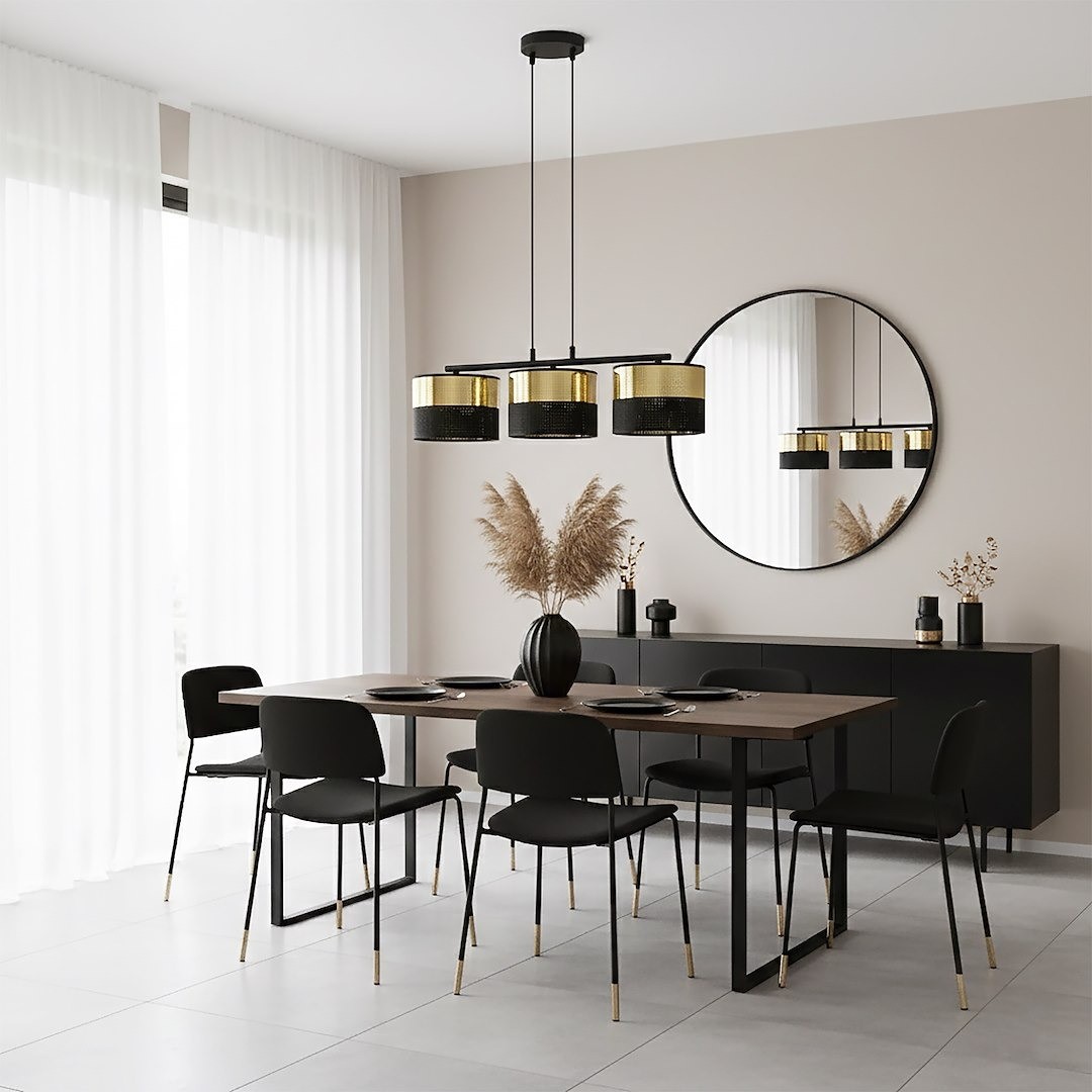 Lampa wisząca Lux 3xE27 w kolorze czarnym z złotymi kloszami, zawieszona na cienkim kablu. Widoczna w nowoczesnej jadalni z drewnianym stołem i czarnymi krzesłami. Tło w jasnym odcieniu szarości z dużym lustrem.