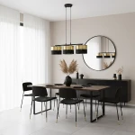 Lampa wisząca Lux 3xE27 w kolorze czarnym z złotymi kloszami, zawieszona na cienkim kablu. Widoczna w nowoczesnej jadalni z drewnianym stołem i czarnymi krzesłami. Tło w jasnym odcieniu szarości z dużym lustrem.