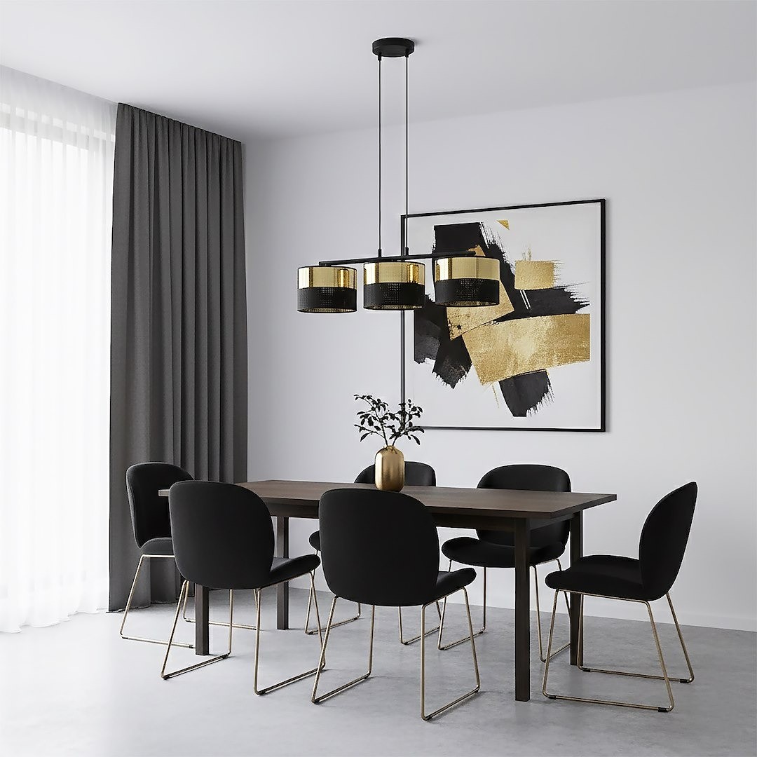 Lampa wisząca Lux 3xE27 w kolorze czarnym i złotym, z trzema okrągłymi kloszami. Zawieszona nad drewnianym stołem w nowoczesnej jadalni, otoczona czarnymi krzesłami na metalowych nogach. W tle jasne zasłony i abstrakcyjny obraz.