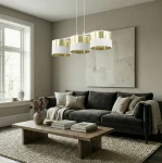 Lampa wisząca Lux 3xE27 w białych i złotych odcieniach, z trzema cylindrycznymi kloszami, zawieszona nad drewnianym stolikiem w nowoczesnym salonie. Tło w jasnych odcieniach, z kanapą i dekoracjami w neutralnych kolorach.