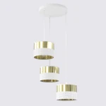 Lampa wisząca Lux w kolorze białym i złotym, z trzema okrągłymi kloszami. Klosze mają perforowaną dolną część i gładką, metaliczną górę. Produkt zawieszony na białych linkach z okrągłym sufitem. Idealna do nowoczesnych wnętrz.