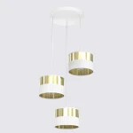 Lampa wisząca Lux z trzema abażurami w białym i złotym kolorze, z metalowymi, perforowanymi detalami. Ułożona w pionie, zawieszona na białym stelażu. Abażury cylindryczne, z białymi dolnymi częściami i złotymi górnymi.
