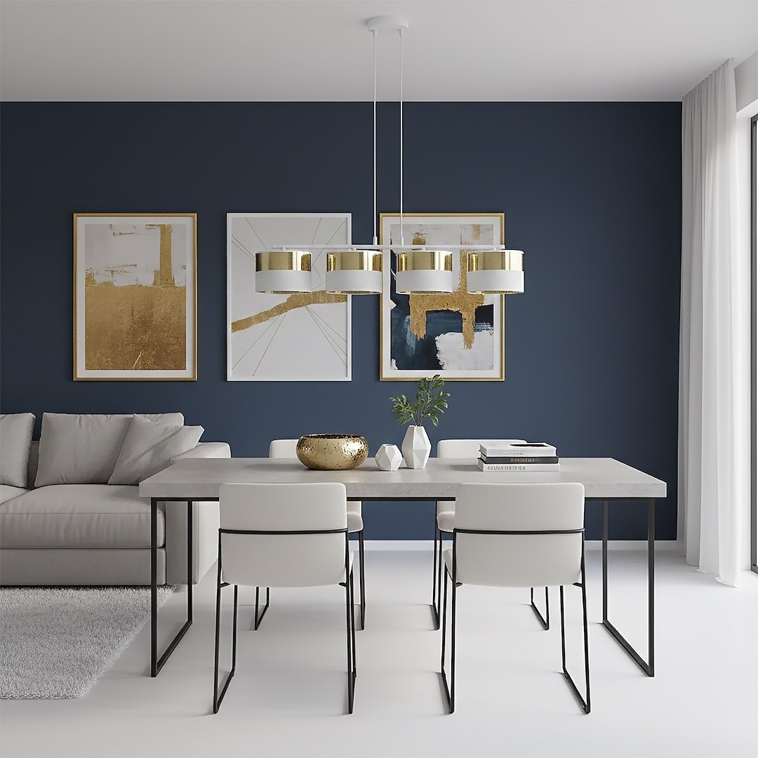 Lampa wisząca Lux 4xE27 w kolorze białym i złotym, z czterema okrągłymi kloszami, zawieszona nad stołem w jasnym wnętrzu. Otoczenie z szaro-białą sofą i nowoczesnymi obrazami na granatowej ścianie, stół z metalowymi nogami i białymi krzesłami.