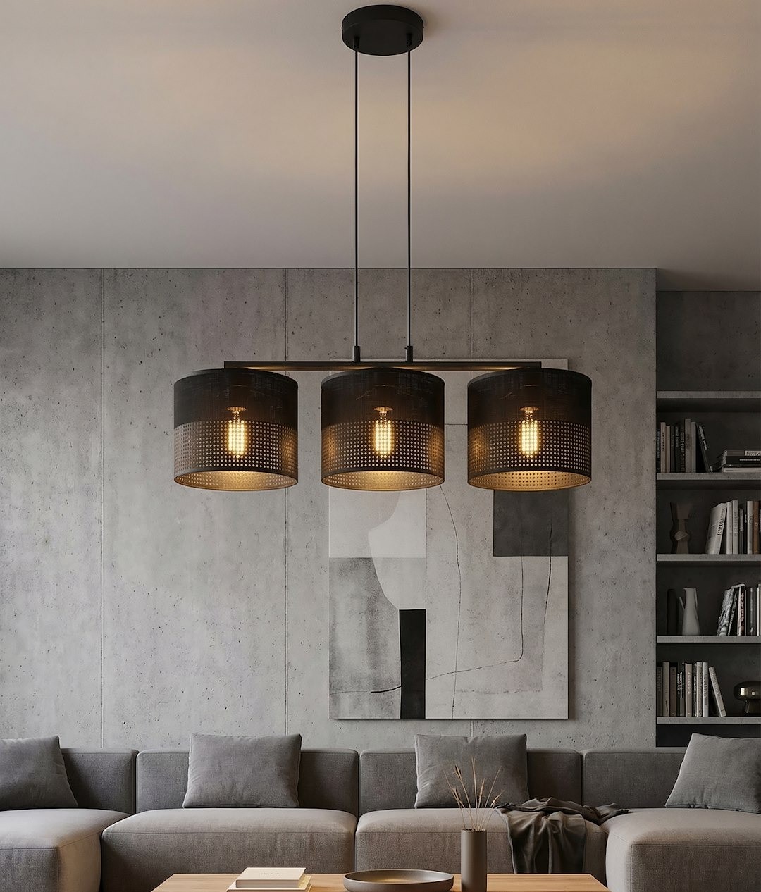 Czarna lampa wisząca Karbon z trzema kloszami E27, zawieszona na dwóch cienkich linkach. Klosze mają perforowaną strukturę, a w środku widoczne żarówki. Tło stanowi nowoczesny salon z szaro-beżową sofą i betonową ścianą.