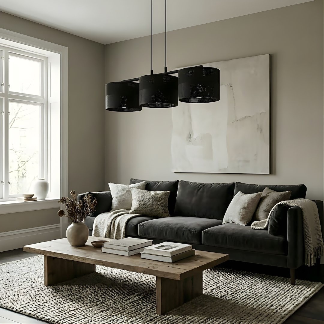 Lampa wisząca Karbon 3xE27 w kolorze czarnym, składająca się z trzech cylindrycznych kloszy, zawieszona na długich linkach. Produkt znajduje się nad drewnianym stołem w nowoczesnym wnętrzu z szarymi ścianami i kanapą, tworząc elegancką aranżację.