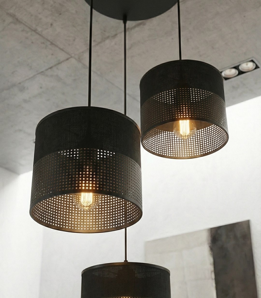 Lampa wisząca Karbon 3xE27 w kolorze czarnym z trzema okrągłymi kloszami z perforowanego materiału, zawieszona na długich linkach. Źródła światła widoczne wewnątrz kloszy, w industrialnym stylu, zawieszona na szarym tle.