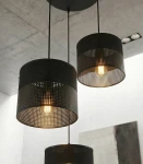 Lampa wisząca Karbon 3xE27 w kolorze czarnym z trzema okrągłymi kloszami z perforowanego materiału, zawieszona na długich linkach. Źródła światła widoczne wewnątrz kloszy, w industrialnym stylu, zawieszona na szarym tle.